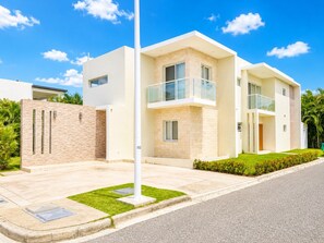 A modern two-story residential building with a flat roof, large windows, and a balcony. - 5bd Corner Lot Villa|Private Pool, Sleeps up to 14 (Sosúa)
