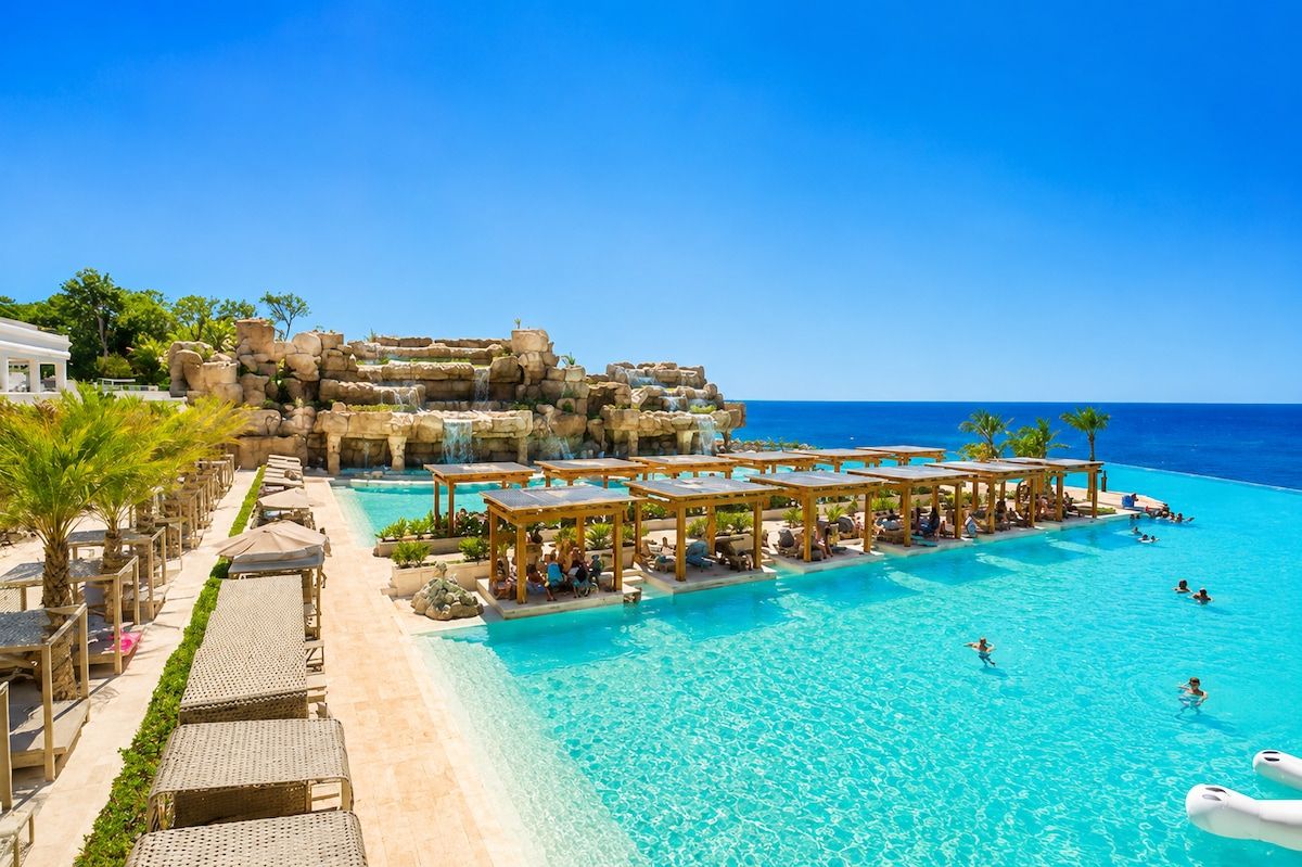 Un resort con una piscina grande, sillas de descanso y un paisaje rocoso de fondo.