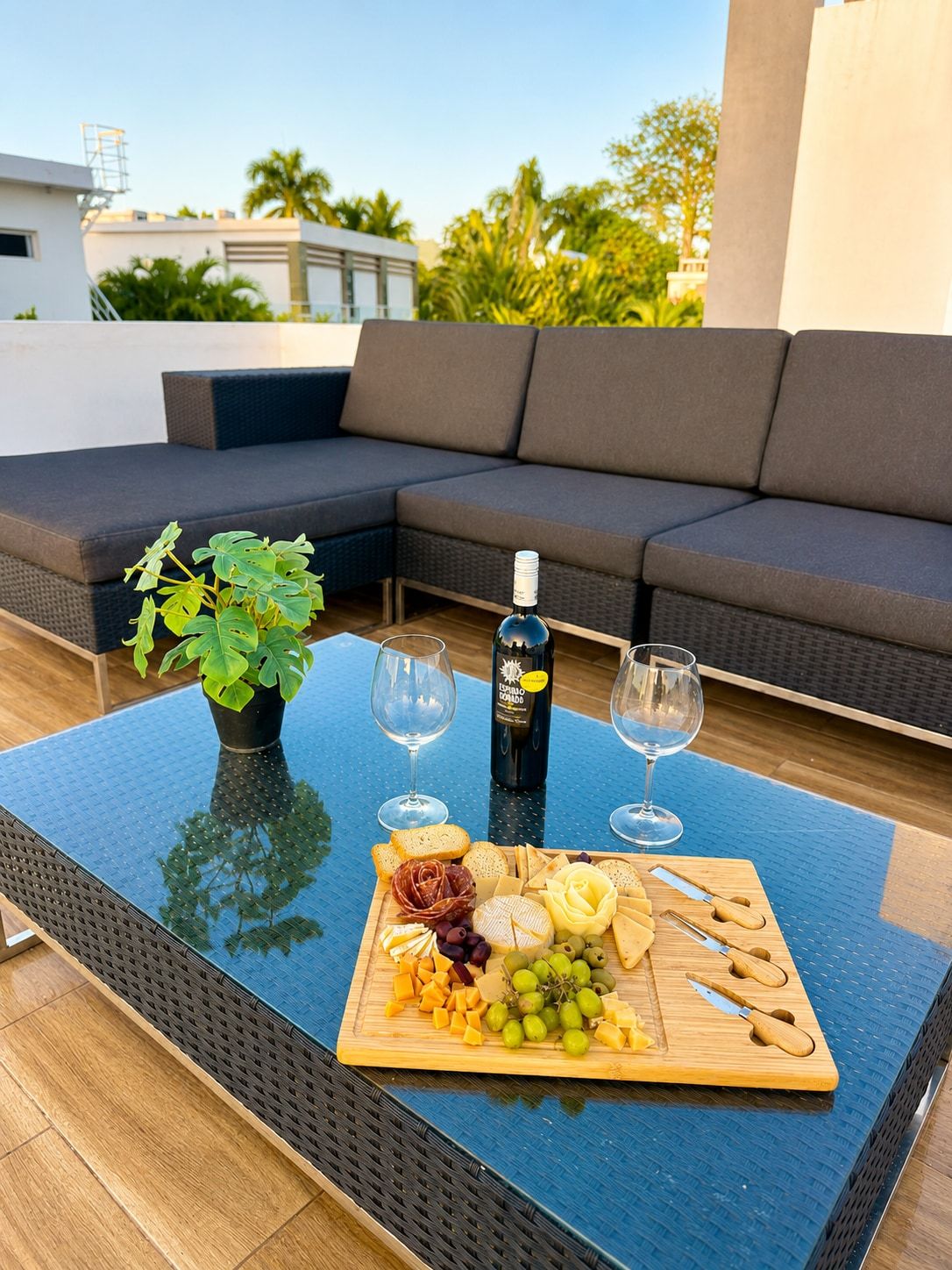 Une terrasse sur le toit, avec une table à manger dressée pour un repas, comprenant une bouteille de vin, des verres et une planche de charcuterie garnie de fromage, de raisins et de différentes sortes de viandes.