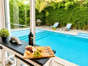 A poolside bar with a selection of cheeses, grapes, and a bottle of wine, overlooking a pool and a lush green garden. - Sleeps up to 9 | Family Retreat, Pool & Jacuzzi (Sosúa)