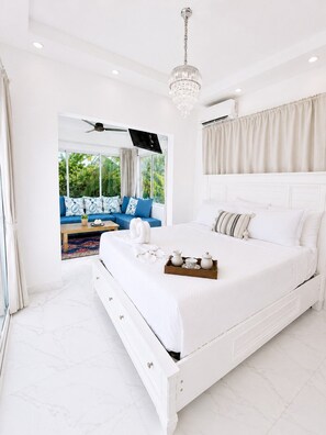 A bedroom with a large bed, a ceiling fan, a chandelier, and a view of greenery outside. - Sleeps up to 9 | Family Retreat, Pool & Jacuzzi (Sosúa)