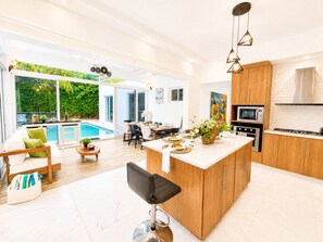 A modern kitchen with a central island, wooden cabinets, and a dining area with a pool view. - Sleeps up to 9 | Family Retreat, Pool & Jacuzzi (Sosúa)