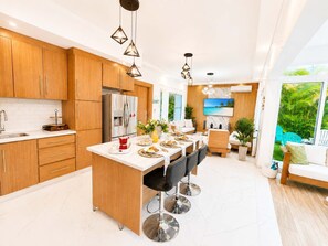 A modern kitchen with wooden cabinets, a stainless steel refrigerator, and a dining area with a bar stool. - Sleeps up to 9 | Family Retreat, Pool & Jacuzzi (Sosúa)