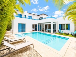 Een modern huis met twee verdiepingen, een zwembad, buitenmeubels en een terras.