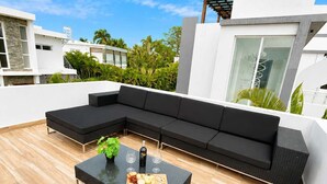 Ein moderner Außenbereich zum Sitzen mit einer Eckcouch und einem Couchtisch, umgeben von einer Holzterrasse.