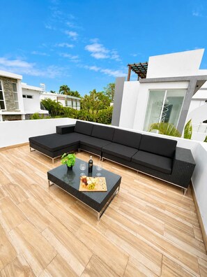 A modern outdoor seating area with a sectional sofa and a coffee table, surrounded by a wooden deck. - Sleeps up to 9 | Family Retreat, Pool & Jacuzzi (Sosúa)
