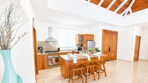 A modern kitchen with wooden cabinets, a central island with stools, and a large window. - Private Pool Villa | Large Yard & Sleeps up to 9 (Sosúa)