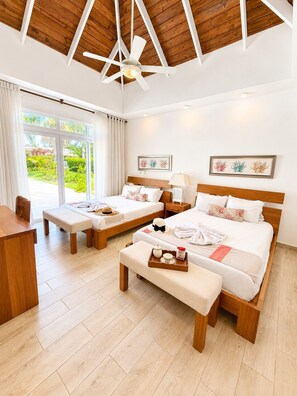 Ein Hotelzimmer mit zwei Betten, einem Schreibtisch, einer Bank und einem Deckenventilator.
