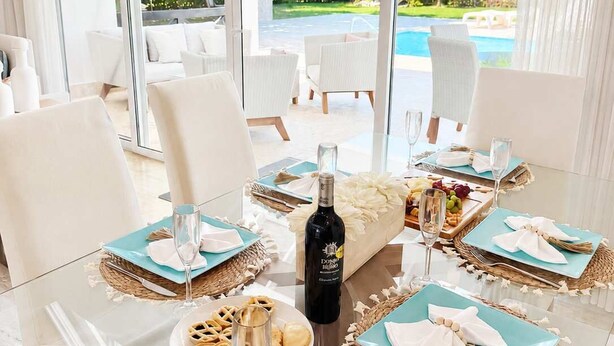 A dining area with a glass table, white chairs, and a view of a pool and greenery outside. - Private Pool Villa | Large Yard & Sleeps up to 9 (Sosúa)