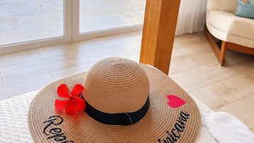 A straw hat with embroidered text on a textured surface, a white towel, and a view of a pool and greenery through a glass door.