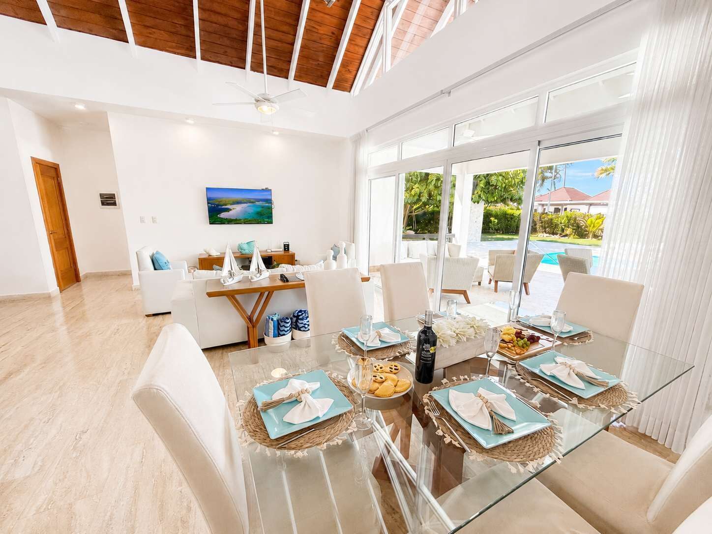 A modern dining area with a glass table, white chairs, and a view of the outdoors.
