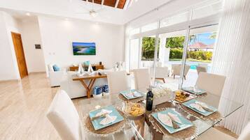 A modern dining area with a glass table, white chairs, and a view of the outdoors.