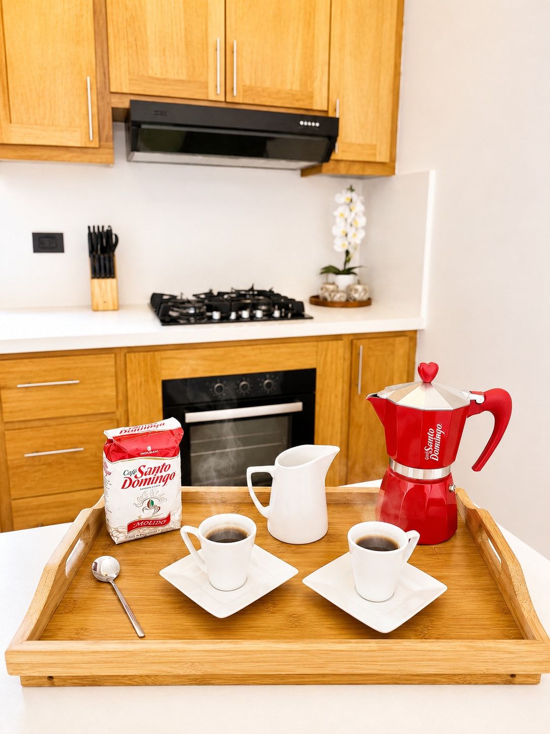 Una cocina con armarios de madera, estufa a gas, horno y una bandeja con cafetera, tazas y un paquete de café.
