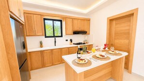 A modern kitchen with wooden cabinets, a built-in oven, and a breakfast setup on the island. - Modern Villa | Pool, Terrace & Sleeps up to 8 (Sosúa)