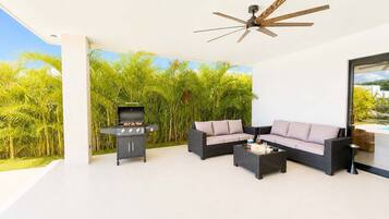A covered outdoor area with a grill, a sofa, and a ceiling fan.