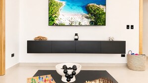 A modern living room with a flat-screen TV mounted on the wall, a black entertainment unit below, and a coffee table with a chess set and a bowl of black and white balls. - Modern Villa | Pool, Terrace & Sleeps up to 8 (Sosúa)