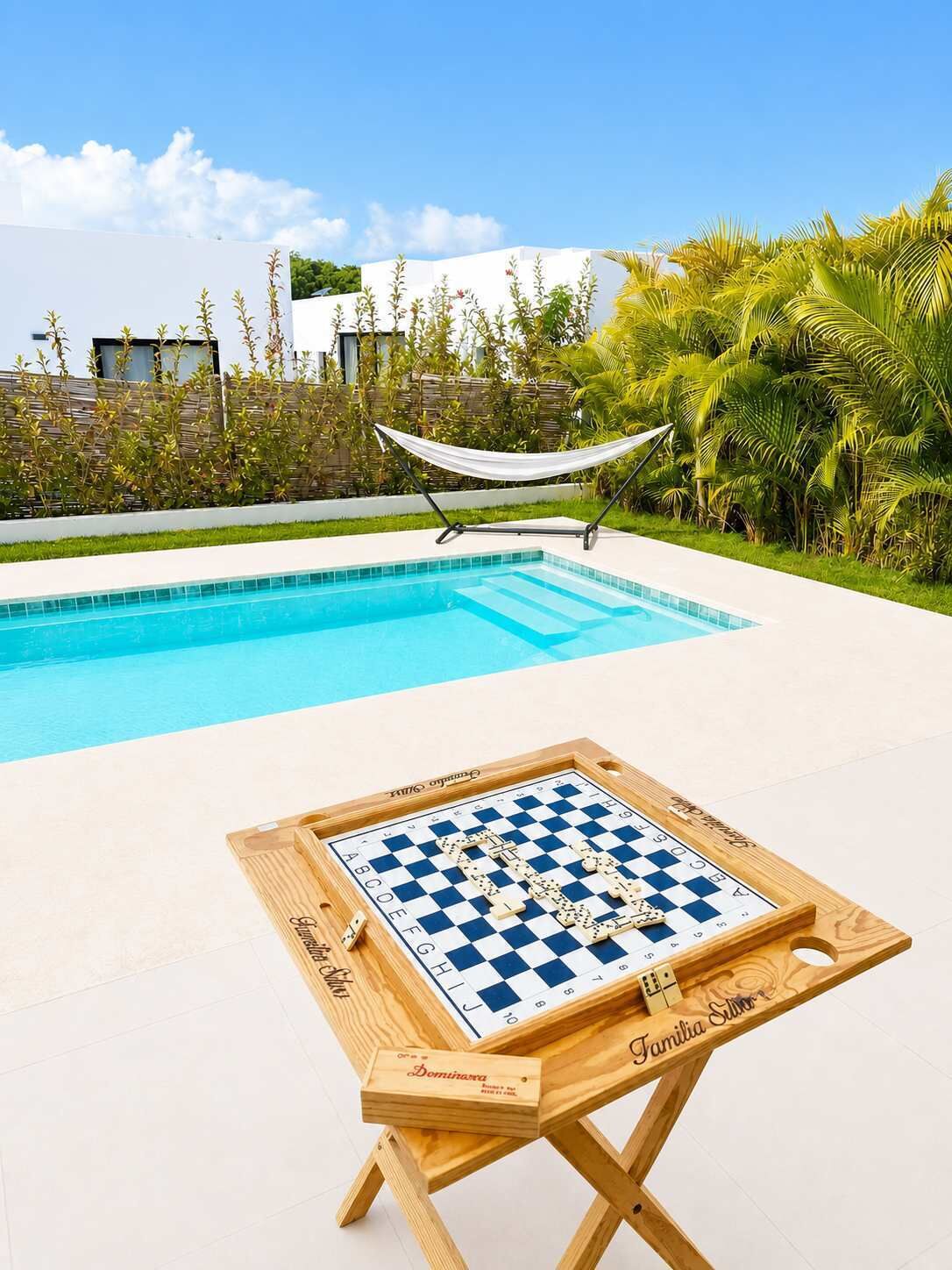 A poolside area with a checkered board game table, a hammock, and a pool.