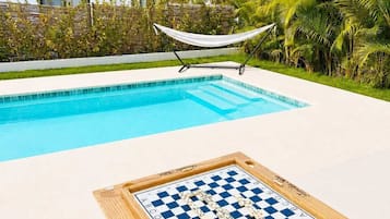 A poolside area with a checkered board game table, a hammock, and a pool.