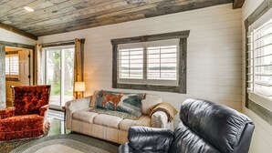 A cozy living room with a wooden ceiling, a sofa, a red armchair, and a window with blinds. - Cozy Cabin on Big Pine Lake w/ Dock & Fire Pit! (New York Mills)