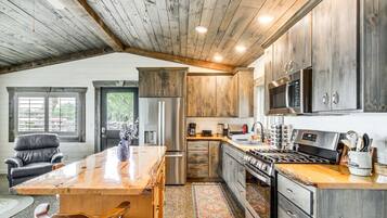 Une cuisine spacieuse avec des meubles en bois, un grand îlot central, des appareils électroménagers en acier inoxydable et une vue sur l’extérieur.