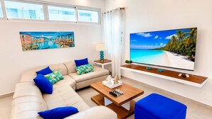 A modern living room with a sofa set, a coffee table, a TV mounted on the wall, and a painting of a beach scene. - Family Villa | Bunk Room, Pool & Up to 12 Guests (Sosúa)