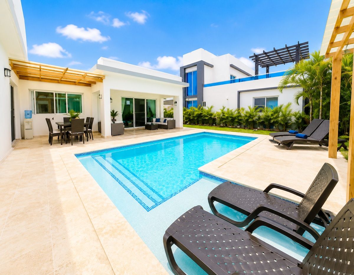 A modern outdoor pool area with lounge chairs, a dining set, and a covered patio.