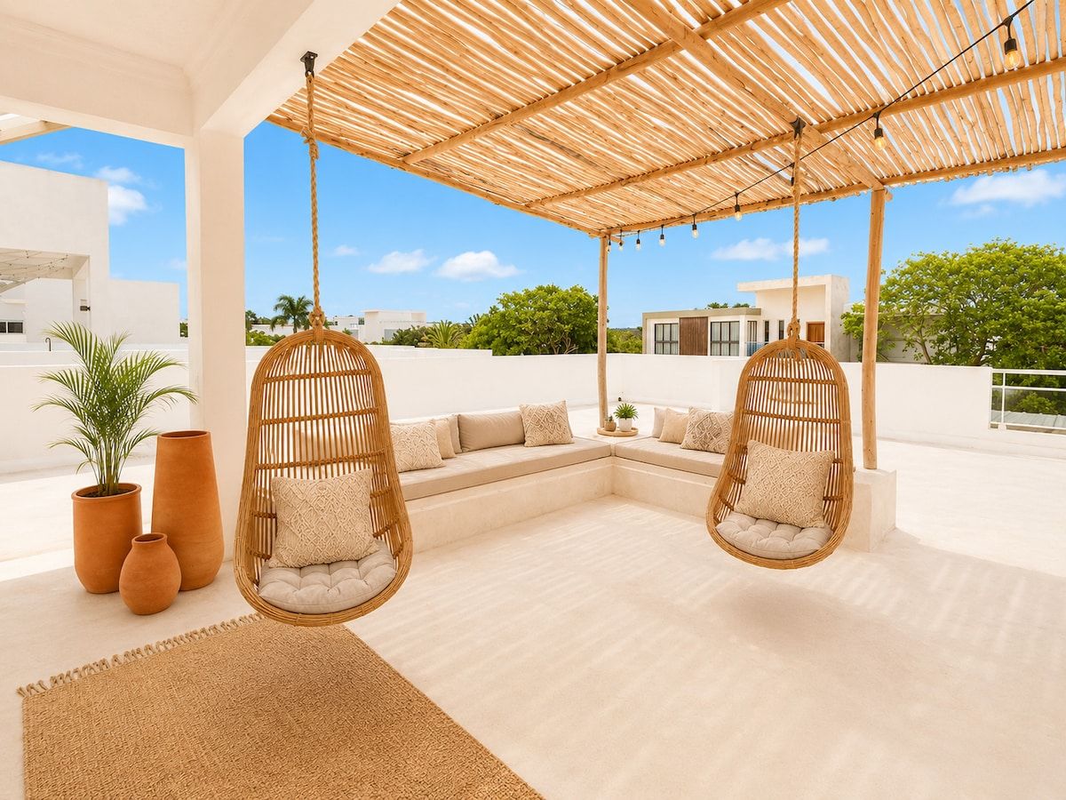 A modern outdoor seating area with two wicker chairs, a woven ceiling, and a view of the surrounding buildings.