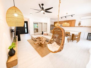 A modern living room with a hanging chair, a wooden coffee table, and a dining area with wooden chairs. - Boho Retreat |Pool Cabana, Terrace Lounge, Rooftop (Sosúa)