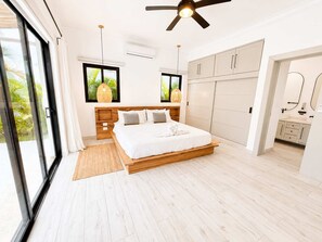 A bedroom with a bed, wooden headboard, bedside tables, a ceiling fan, and a view of greenery through the window. - Boho Retreat |Pool Cabana, Terrace Lounge, Rooftop (Sosúa)