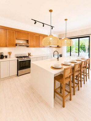 A modern kitchen with wooden cabinets, a central island, and pendant lighting. - Boho Retreat |Pool Cabana, Terrace Lounge, Rooftop (Sosúa)