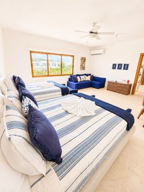Une chambre à coucher avec un lit, un canapé bleu, une commode en bois, un ventilateur de plafond et une fenêtre donnant sur un beau paysage.