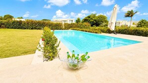 Une piscine sous un ciel bleu azur, entourée de verdure et bordée d’une terrasse carrelée.