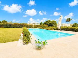 A swimming pool with a clear blue sky, surrounded by greenery and a tiled deck. - Sleeps up to 22 | Estate Pool 6bd Villa Corner Lot (Sosúa)