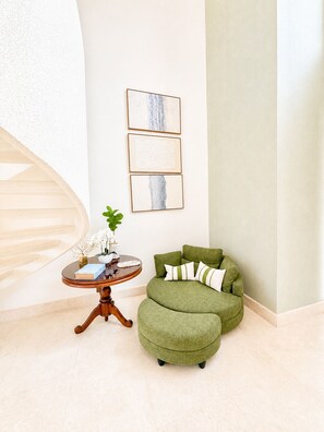 Une pièce comprenant un canapé vert recouvert de tissu, une table ronde en bois ornée d’une plante, et trois œuvres d’art encadrées accrochées au mur.