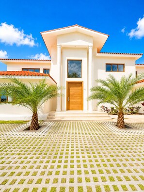 A modern building with a central entrance, two palm trees, and a patterned pavement. - Sleeps up to 22 | Estate Pool 6bd Villa Corner Lot (Sosúa)