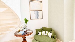 Une pièce comprenant un canapé vert recouvert de tissu, une table ronde en bois ornée d’une plante, et trois œuvres d’art encadrées accrochées au mur.
