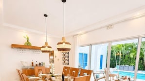 Un espace repas avec une table en verre, des chaises en bois et des luminaires suspendus.