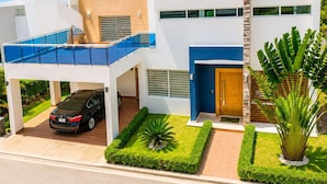Une maison moderne à deux étages, avec une voiture garée dans l’allée, un patio couvert et une pelouse bien entretenue.