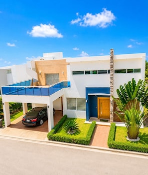 Une maison moderne à deux étages, avec une voiture garée dans l’allée, un patio couvert et une pelouse bien entretenue.