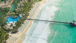 Vista aérea de un complejo turístico con playa, un muelle largo y una zona de piscina.