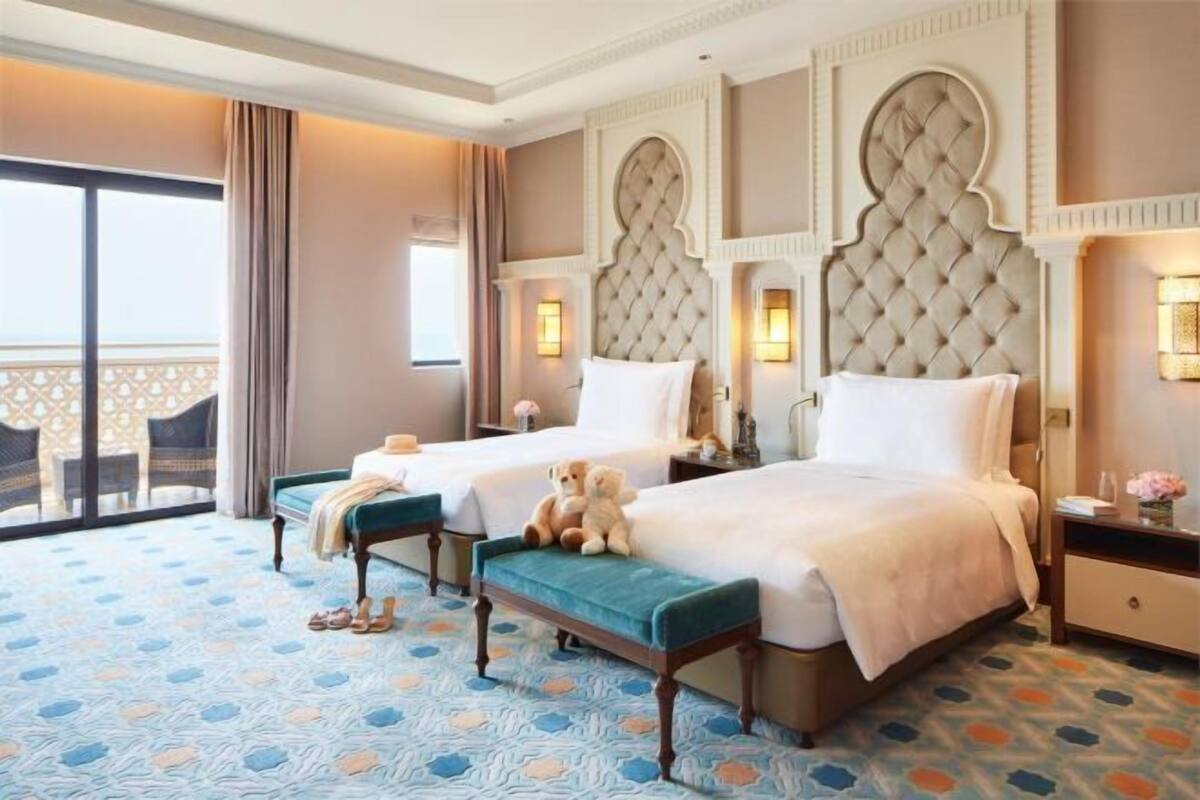 Habitación de hotel con dos camas, un balcón y una alfombra estampada.