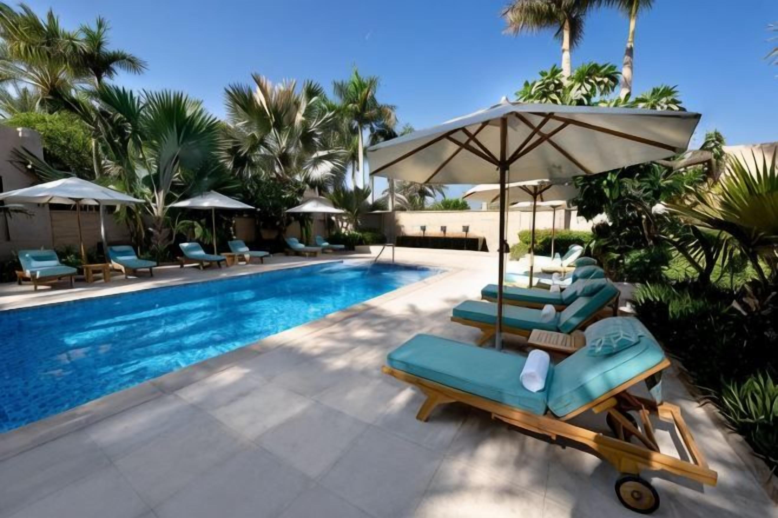 Une piscine entourée de palmiers, avec des chaises longues et des parasols.