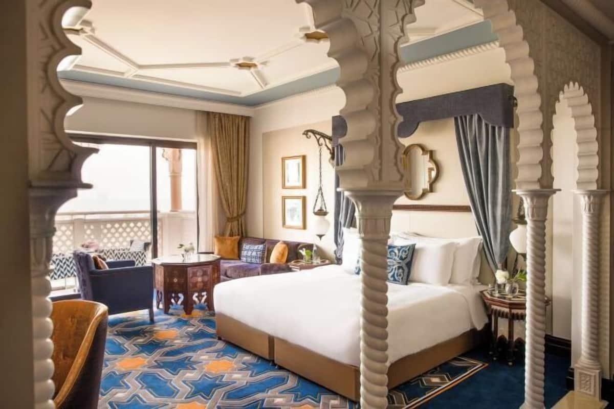 Habitación de hotel con una cama grande, una mesita pequeña, una silla y un balcón con vistas.