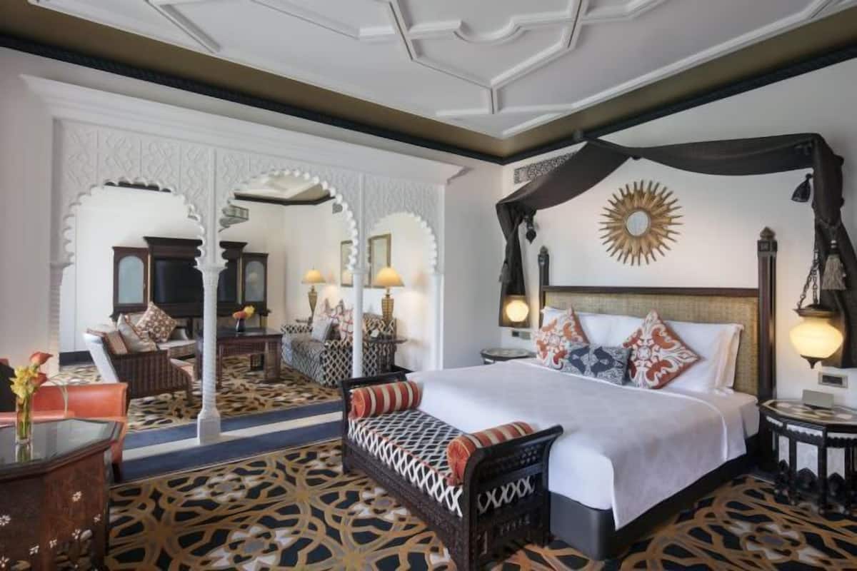 Habitación de hotel con una cama grande, un área de descanso con un banco, un sofá y una mesa de comedor.