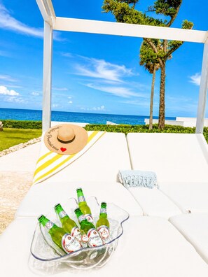 A beachside lounge with a clear view of the ocean, a straw hat, and a bowl of beer bottles. - Oceanfront Paradise | Cliffside Spa & Pool in SOV (Sosúa)