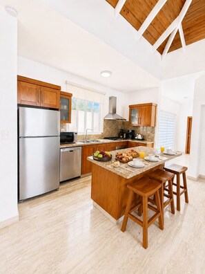 A modern kitchen with a central island, stainless steel appliances, wooden cabinets, and a large window providing natural light. - Oceanfront Paradise | Cliffside Spa & Pool in SOV (Sosúa)