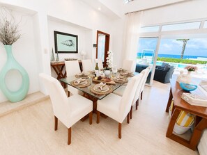 A dining area with a glass table, white chairs, and a view of the ocean. - Oceanfront Paradise | Cliffside Spa & Pool in SOV (Sosúa)
