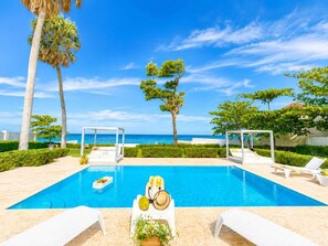 A swimming pool with lounge chairs and umbrellas, surrounded by palm trees and a view of the sea. - Oceanfront Paradise | Cliffside Spa & Pool in SOV (Sosúa)
