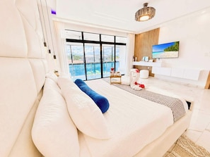 Een moderne slaapkamer met een groot bed, uitzicht op zee, en een badkamer met een houten wastafelmeubel.