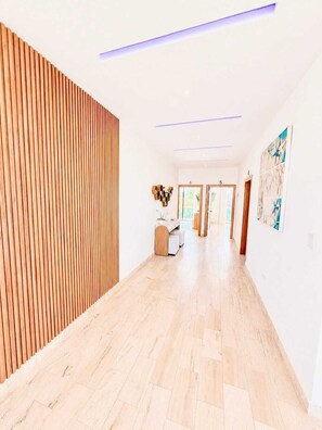 Een gang met houten latten aan één kant, een receptiebalie met een bloevas en een muur met kunstwerken.